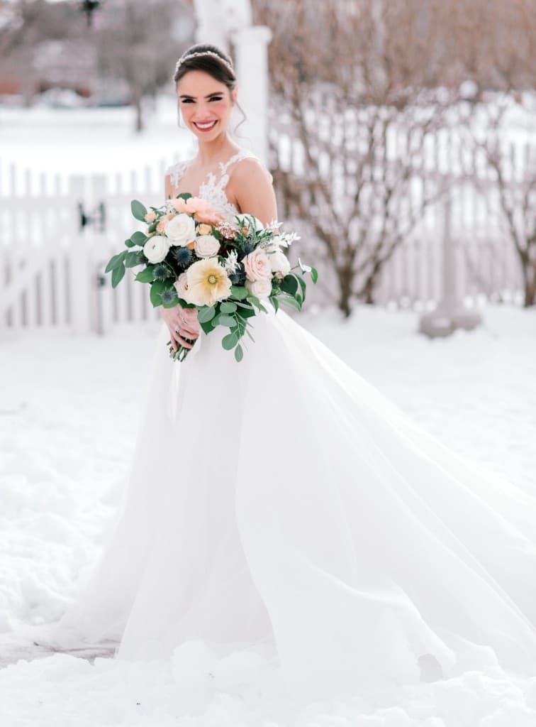 Bride holding bouquet standing in snow at The Commons 1854 winter wedding