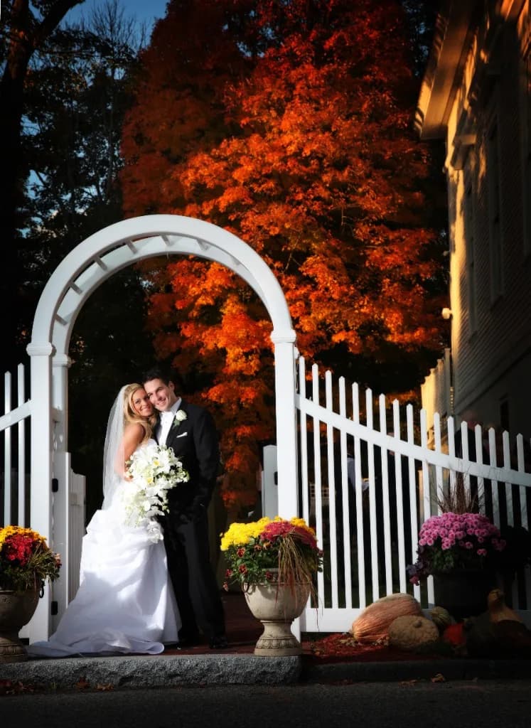 Couple under white arch gate with blazing fall foliage at The Commons 1854