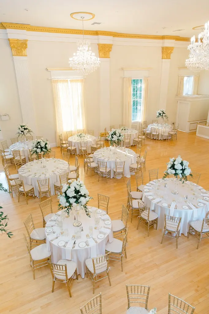 Grand ballroom interior at The Commons 1854 — Swarovski chandeliers, gold Chiavari chairs, white florals